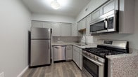 This single-floor residence offers a thoughtfully designed layout that balances functionality and comfort across its key living spaces. The kitchen is a standout feature, equipped with a full suite of stainless steel appliances including a gas range, over-the-range microwave, dishwasher, and full-size refrigerator. Grey shaker-style cabinetry extends to the upper walls, providing generous storage, while speckled granite countertops offer ample prep space. Wood-look plank flooring completes the kitchen's polished appearance.

The open living area transitions seamlessly from the kitchen and is anchored by a striking corner fireplace with a sleek black surround, adding both warmth and visual interest. Soft carpeting extends throughout the living and bedroom areas. A ceiling fan provides additional comfort, while a large sliding glass door floods the space with natural light and offers views of the outdoors.

The bedroom is well-sized with its own ceiling fan, a closet, and a window dressed with vertical blinds. The bathroom features clean white finishes, light tile flooring, and granite countertops. A dedicated laundry room with a full-size washer and dryer adds everyday convenience to this move-in-ready space.