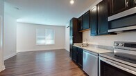 Located at 500 Bank St in New London, Connecticut, this single-floor unit offers a clean, modern design with thoughtful finishes throughout. The open-concept layout seamlessly connects the kitchen and living area, creating a bright and functional space filled with natural light from a large window fitted with blinds.

The kitchen is a standout feature, equipped with dark espresso-toned shaker-style cabinetry that extends to the ceiling for generous storage. Granite countertops provide a durable and attractive work surface, complemented by a stainless steel undermount sink and a full suite of stainless steel appliances, including a refrigerator, electric range, microwave, and dishwasher. The warm hardwood-style flooring runs continuously from the kitchen into the open living area, enhancing the cohesive feel of the space.

The hallway area offers access to multiple doors, including a barn-style sliding door that adds a modern architectural touch. The bathroom features classic black-and-white hexagon tile flooring, a vanity with a large mirror, and neutral wall tones that create a clean, timeless aesthetic.

Throughout the unit, recessed lighting, crisp white walls, and clean baseboards contribute to a polished, move-in-ready atmosphere well-suited for comfortable everyday living.