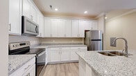 Located in Bowling Green, KY, this well-appointed single-story home offers three bedrooms, two bathrooms, and a thoughtfully designed layout. The open kitchen is a standout feature, showcasing white shaker cabinets extending to the ceiling, granite countertops, and a central island with a built-in sink — all complemented by a full suite of stainless steel appliances including a range, over-the-range microwave, and refrigerator. Light wood-look LVP flooring flows consistently throughout the home, tying each room together with a clean, modern aesthetic. Crown molding adds a refined touch to the living room, which features a ceiling fan and natural light from a window and glass door leading outside. The bedrooms are comfortably sized, with the primary bedroom offering closet access and a window with natural light. Both bathrooms are finished with granite-topped white vanities and LVP flooring, with one featuring a full tub-shower combination. A dedicated laundry room includes washer/dryer hookups and a wall-mounted drying rack, adding everyday convenience. Neutral warm-toned walls throughout create a welcoming and versatile atmosphere suitable for a variety of furnishing styles.