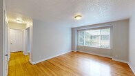 Located at 1610 NE 66th Ave in Portland, OR, this single-floor unit offers four bedrooms, one bathroom, a kitchen, and a connecting hallway within a compact and efficiently organized layout. Warm-toned hardwood floors run throughout the living spaces and bedrooms, contributing a cohesive and inviting aesthetic. Neutral gray walls and white trim provide a clean, versatile backdrop across all rooms. The spacious primary bedroom includes views of surrounding greenery through large windows fitted with blinds, creating a bright and peaceful environment. The additional bedrooms each feature hardwood flooring and natural light, with several offering outdoor views of mature trees. The kitchen is equipped with white cabinetry, laminate countertops, a coil-burner electric range, and a window above the sink that allows natural light to fill the space. The bathroom features classic hexagonal tile flooring and a full tub-shower combination in a crisp white finish. A hallway connects the main areas efficiently. The unit presents a straightforward, functional design with consistent finishes throughout, making it a well-organized multi-bedroom space in a residential Portland neighborhood.