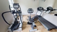 This dedicated fitness space is designed to support a comprehensive cardio workout routine, offering a focused and functional environment for exercise. The room is outfitted with professional-grade True Fitness equipment, including an elliptical trainer, a recumbent stationary bike, and a treadmill — providing a well-rounded selection of low-impact and higher-intensity cardio options. The light-toned tile flooring is both practical and easy to maintain, offering a sturdy surface suited for exercise equipment. The walls are finished in a clean, neutral tone that contributes to a bright and motivating atmosphere. The layout is thoughtfully arranged to allow comfortable access to each machine without overcrowding the space. Natural light appears to be present, enhancing the overall openness of the room. Whether used for daily cardio sessions or as part of a broader fitness routine, this space delivers a convenient and well-appointed workout environment all on a single floor.
