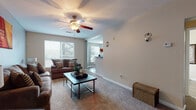 This single-floor residence offers a practical and comfortable layout across two bedrooms and two bathrooms. The living room is a welcoming space featuring plush carpeting, a ceiling fan with light fixture, and large windows fitted with blinds that allow generous natural light. The room comfortably accommodates a full seating arrangement alongside a coffee table, creating an inviting atmosphere for relaxing or entertaining.

The kitchen is well-appointed with white cabinetry, dark granite-style countertops, white appliances including a range, dishwasher, and refrigerator, and hardwood-style flooring. Adjacent to the kitchen is a distinct dining area defined by a curved bay window configuration, providing views to the outdoors and additional natural light. This space features the same durable hardwood-style flooring.

The primary bedroom is generously sized with carpeting, a ceiling fan, and a window offering outdoor views. The second bedroom is a comfortable, carpeted room also equipped with a ceiling fan. Both bathrooms include a tub-shower combination. A dedicated in-unit laundry area houses a full-size washer and dryer with overhead shelving for added convenience.