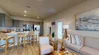 This single-floor residence exudes a relaxed, coastal aesthetic throughout its thoughtfully designed layout. The open-concept living and kitchen area serves as the heart of the home, where light wood-look flooring and neutral wall tones create a warm, welcoming atmosphere. Large windows in the living room invite abundant natural light, complementing the space's airy feel.

The kitchen is well-equipped with stainless steel appliances, including a French door refrigerator, electric range, and built-in microwave. Gray shaker-style cabinetry extends to the ceiling, paired with a subtle subway tile backsplash and crisp white countertops. A peninsula with seating provides a casual dining option alongside a dedicated dining nook featuring a window with sheer curtains.

The bedrooms are comfortably sized, each featuring light wood-look flooring, ceiling fans, and windows that bring in natural light. The soft, neutral color palettes give each room a serene, restful character. The bathroom is finished with a gray double-vanity, white countertop, glass-enclosed walk-in shower, and matching wood-look tile flooring, maintaining a cohesive design throughout. An exterior door off the living area provides convenient access to the outdoors.