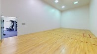 Located at 4909 E Upriver Dr in Spokane, Washington, this single-floor recreational facility offers two distinct, purpose-built areas designed for active use. The centerpiece of the space is a regulation racquetball court, characterized by its smooth hardwood flooring with clearly marked red boundary lines, bright white enclosed walls, and high ceilings illuminated by recessed overhead lighting panels. The clean, open design of the court provides an ideal environment for competitive or recreational play. Adjacent to the court is a well-appointed fitness room outfitted with a diverse range of exercise equipment, including a treadmill, elliptical trainer, stationary bike, and a multi-station cable weight machine. The fitness area features durable carpeted flooring, a large wall-mounted mirror that enhances the sense of space, and multiple windows that allow natural light to fill the room. A wall-mounted water fountain provides convenient hydration access. The fitness room also includes a seating bench and climate control units for year-round comfort. Together, these two areas create a comprehensive, functional fitness and recreation facility suited for a variety of athletic and wellness activities.