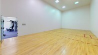 Located at 4909 E Upriver Dr in Spokane, Washington, this single-floor recreational facility offers two distinct, purpose-built areas designed for active use. The centerpiece of the space is a regulation racquetball court, characterized by its smooth hardwood flooring with clearly marked red boundary lines, bright white enclosed walls, and high ceilings illuminated by recessed overhead lighting panels. The clean, open design of the court provides an ideal environment for competitive or recreational play. Adjacent to the court is a well-appointed fitness room outfitted with a diverse range of exercise equipment, including a treadmill, elliptical trainer, stationary bike, and a multi-station cable weight machine. The fitness area features durable carpeted flooring, a large wall-mounted mirror that enhances the sense of space, and multiple windows that allow natural light to fill the room. A wall-mounted water fountain provides convenient hydration access. The fitness room also includes a seating bench and climate control units for year-round comfort. Together, these two areas create a comprehensive, functional fitness and recreation facility suited for a variety of athletic and wellness activities.