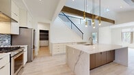 Located at 28790 Addison Court in Pepper Pike, Ohio, this contemporary two-story home offers a thoughtfully designed layout across two generously sized floors. The main level impresses immediately with soaring vaulted ceilings accented by rich dark wood beams and a dramatic open staircase with sleek black metal railings. The kitchen is a standout centerpiece, featuring an expansive waterfall-edge marble island, warm walnut cabinetry, tall white upper cabinets, a mosaic tile backsplash, a stainless steel range with a wall-mounted hood, and pendant gold accent lighting. Light hardwood-style flooring flows throughout the main level, complementing the bright, airy atmosphere. The living room opens to the outdoors through large windows and French doors, flooding the space with natural light and views of the surrounding greenery. A stylish half bath with gray walls, a pedestal sink, and a round mirror serves the main floor. Two dedicated laundry rooms offer added convenience. Upstairs, the carpeted hallway and bedrooms provide a quiet retreat, including a well-proportioned primary bedroom and walk-in closets. The upper level also features a bright open landing area. The attached two-car garage completes this polished, move-in-ready home.
