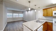 Located at 200 N Harvey Ave in the heart of Oklahoma City, this one-bedroom, one-bathroom unit offers a well-organized, single-floor layout designed for efficient and comfortable living. The open-concept kitchen and living area form the core of the space, creating a seamless flow between cooking and relaxing. The kitchen is well-appointed with warm honey-toned wood cabinetry, ample upper and lower storage, a peninsula countertop with a double stainless steel sink, and white appliances including a refrigerator, electric range, microwave, and dishwasher. Light tile flooring in the kitchen contrasts with the rich, dark hardwood-style flooring that extends throughout the living areas. The living room is bathed in natural light from a wide bank of windows fitted with horizontal blinds, offering views of the surrounding cityscape. Pendant lighting over the kitchen peninsula and track lighting add functional illumination throughout. The spacious primary bedroom features the same hardwood-style flooring and large windows that invite abundant natural light. The bathroom is clean and functional, with tile flooring, a vanity with wood cabinetry, and a full tub-shower combination. Additional spaces include a dedicated closet, entrance area, and utility room, ensuring practical everyday storage and convenience.