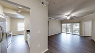 This single-floor residence offers a thoughtfully designed layout that balances open living spaces with functional, well-defined rooms. The entryway opens into a generous common area finished with rich, dark-toned hardwood-style flooring that flows consistently throughout the home, creating a cohesive and polished aesthetic.

The living room is a standout space, featuring crown molding, a ceiling fan, and a full-width sliding glass door with vertical blinds that floods the room with natural light and provides access to an outdoor view. The kitchen is efficiently designed in a galley style, equipped with stainless steel appliances including a refrigerator, electric range, and built-in microwave. White cabinetry with modern brushed-nickel hardware pairs elegantly with dark granite countertops, while track lighting illuminates the workspace.

The bedrooms are comfortably sized, each outfitted with ceiling fans and durable flooring. One bedroom includes a walk-in closet with built-in shelving, offering generous storage. A secondary bedroom features a large window that invites natural light and an outdoor view of surrounding greenery.

The bathroom is well-appointed with a dark granite vanity countertop, white cabinetry, a large mirror, a tiled shower/tub combination, and wood-style flooring. Neutral, warm-toned walls throughout the home contribute to a calm and inviting ambiance.