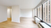 Located at 233 E Wacker Drive in Chicago's vibrant Streeterville neighborhood, this one-bedroom, one-bathroom residence offers a thoughtfully designed layout across a single floor. The combined living and dining area serves as the heart of the unit, characterized by expansive floor-to-ceiling windows that frame striking views of the Chicago skyline and the Chicago River below, flooding the space with natural light. Light wood flooring runs throughout, complementing the clean, neutral palette of white walls and trim. Track lighting accents the living area, adding functional illumination.

The kitchen is well-appointed with white shaker-style cabinetry, white countertops, and a full suite of stainless steel appliances including a refrigerator, range, microwave, and dishwasher, all set on matching light wood flooring. A hallway connects the main living areas to the private bedroom, which offers comfortable proportions and access to two closets, providing ample storage. The bathroom features a classic white tiled tub-shower combination with chrome fixtures, maintaining the unit's clean, bright aesthetic. The overall design is modern and understated, emphasizing natural light, city views, and efficient use of space throughout.