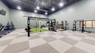 Located at 400 Mallard Creek Rd in St. Matthews, Kentucky, this single-floor fitness center offers a generously sized, open layout designed to accommodate a wide range of workout disciplines. The facility is defined by its soaring exposed ceiling with industrial-style high-bay lighting, light green square-tiled walls, and a combination of modular carpet tile and synthetic turf flooring throughout.

The cardio zone features a row of treadmills, elliptical trainers, stair climbers, and a rowing machine, all positioned along the perimeter walls for easy access. Wall-mounted televisions are strategically placed throughout the space to enhance the workout experience. A dedicated strength training area includes multiple selectorized cable machines, weight benches, and a full rack of color-coded bumper plates and barbells.

A central functional training zone is anchored by a multi-purpose rig system equipped with TRX suspension trainers, pull-up bars, and various attachments. This area transitions onto an artificial turf section ideal for sled work, agility drills, and dynamic movement exercises. Interior windows along one wall provide visual connectivity between zones. The facility's high ceilings and broad, unobstructed floor plan create an energizing, professional-grade training environment well-suited for a diverse range of fitness activities.