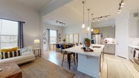 This well-designed two-floor residence offers a thoughtfully planned layout that balances open communal spaces with private retreats. The heart of the home is an open-concept living, dining, and kitchen area bathed in natural light from large windows. Soaring ceilings in the living room create an airy, expansive atmosphere, complemented by light wood-style flooring and ceiling fans throughout. The kitchen is outfitted with sleek gray cabinetry, stainless steel appliances, a subway tile backsplash, and a generous island with a white quartz countertop — ideal for both meal preparation and casual dining. Pendant lighting with gold accents adds a refined touch overhead. The dining area comfortably accommodates a full-sized table and benefits from its own natural light source and track lighting above. The living room features dramatic ceiling height, wide windows, and an arched passageway that adds architectural charm. The primary bedroom is generously proportioned with plush carpeting, while its en-suite bathroom showcases a dual-sink vanity, soaking tub, and a separate shower. A secondary bathroom includes a shower-tub combination. A dedicated home office with ample natural light rounds out the functional offerings of this well-appointed space.