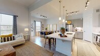 This well-designed two-floor residence offers a thoughtfully planned layout that balances open communal spaces with private retreats. The heart of the home is an open-concept living, dining, and kitchen area bathed in natural light from large windows. Soaring ceilings in the living room create an airy, expansive atmosphere, complemented by light wood-style flooring and ceiling fans throughout. The kitchen is outfitted with sleek gray cabinetry, stainless steel appliances, a subway tile backsplash, and a generous island with a white quartz countertop — ideal for both meal preparation and casual dining. Pendant lighting with gold accents adds a refined touch overhead. The dining area comfortably accommodates a full-sized table and benefits from its own natural light source and track lighting above. The living room features dramatic ceiling height, wide windows, and an arched passageway that adds architectural charm. The primary bedroom is generously proportioned with plush carpeting, while its en-suite bathroom showcases a dual-sink vanity, soaking tub, and a separate shower. A secondary bathroom includes a shower-tub combination. A dedicated home office with ample natural light rounds out the functional offerings of this well-appointed space.