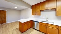 Located at 5541 Bantry Ln in Virginia Beach, VA, this single-floor, two-bedroom, one-bathroom residence offers a efficiently organized layout across a compact footprint. The kitchen serves as a functional highlight, featuring warm honey-toned wood cabinetry extending from floor to ceiling, white countertops, stainless steel appliances including a dishwasher, electric range, and microwave, along with an L-shaped peninsula that provides additional prep and storage space. Light wood-style flooring runs throughout the kitchen area, enhancing the brightness of the space. Both bedrooms are finished with neutral-toned carpet and beige walls, each receiving natural light through windows fitted with blinds. The primary bedroom includes a built-in closet with wood bifold doors, while both rooms feature consistent trim work and overhead ventilation. The bathroom is equipped with a tub-shower combination featuring a grab bar, a toilet, and wall-mounted wood cabinetry for storage, complemented by light flooring that ties the space together. Clean white baseboards and neutral wall tones throughout the residence create a cohesive, understated aesthetic suited for practical everyday living.