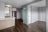 Located on the 7th floor at 245 Main Street in Toronto's east end, this one-bedroom, one-bathroom suite offers a thoughtfully designed layout that makes efficient use of its compact footprint. The interior is finished in a clean, contemporary palette of soft whites and warm wood-toned accents, unified throughout by durable wood-look flooring.

The kitchen is a standout feature, outfitted with a full suite of stainless steel appliances — including a refrigerator, electric range, built-in microwave, and dishwasher — complemented by glossy white cabinetry extending to the ceiling, a subway tile backsplash, and a peninsula that provides added counter space and a casual eating area. The open layout connects the kitchen to the living area, which is brightened by a wide, low-profile window that frames an expansive view of the surrounding Toronto neighbourhood and greenery below.

The bedroom is a cozy, well-defined space, while the bathroom features a full soaker tub with a tiled surround, a modern vanity with a wood-grain cabinet, and warm hardwood flooring. A hallway with a built-in panel storage unit connects the rooms efficiently. The overall ambiance is bright, clean, and move-in ready, reflecting a modern renovation with practical urban living in mind.