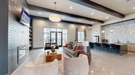 Located at 5425 E Orem Dr in Houston, TX, this thoughtfully designed community amenity space delivers a sophisticated, resort-style experience across a single floor. The open-concept layout flows seamlessly between distinct functional zones, each finished with modern materials and curated décor.

The main lounge area is an inviting focal point, featuring soaring ceilings with bold dark exposed beams, large-format tile flooring, and floor-to-ceiling glass doors that flood the space with natural light and provide views to the exterior. A striking herringbone-tiled fireplace wall, flanked by built-in bookshelves, anchors this area alongside plush seating arrangements.

Adjacent to the lounge, a comfortable sitting room offers light wood-look flooring, tall windows dressed with floor-length drape panels, and clusters of amber-upholstered lounge chairs arranged around sleek white tables — ideal for casual gatherings or quiet relaxation.

The game room provides an energetic counterpoint, equipped with a ping-pong table, foosball table, wall-mounted television, and stylized accent wallcovering, all set against a bright, airy backdrop with ample natural light.

A fully appointed bar and kitchen area rounds out the space, showcasing dramatic marble-look tile walls, dark exposed ceiling beams, a large island with bar seating, pendant lighting, and a stainless steel refrigerator — perfect for hosting and social events.
