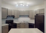 Located at 1100 Walden Legacy Way in Knoxville, Tennessee, this single-floor unit offers a well-designed layout with consistent modern finishes throughout. The kitchen is a standout feature, equipped with gray shaker-style cabinetry, granite-look countertops, and black appliances including a refrigerator, electric range, dishwasher, and a double-basin stainless steel sink. A peninsula with matching countertop extends into the open living area, providing additional workspace and a natural divide between the kitchen and the rest of the unit. Track lighting illuminates the kitchen, while crown molding adds a refined touch to the common areas. Dark hardwood-style flooring runs throughout, offering a cohesive and contemporary aesthetic. A built-in desk nook is conveniently tucked near the kitchen, ideal as a workspace or study area. The bedroom features a ceiling fan, a window with natural light and outdoor views of lush greenery, and access to a generously sized walk-in closet with multi-level wire shelving. The bathroom includes a granite-look vanity countertop with an integrated sink, a large mirror, and a full shower-tub combination. A textured ceiling is consistent throughout the unit, complementing the neutral gray wall tones.