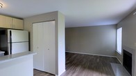 This single-floor space presents a clean, minimalist aesthetic defined by neutral greige wall tones and crisp white trim and baseboards. The flooring throughout is a rich, dark wood-style plank, adding warmth and contrast to the lighter wall palette. The image reveals an open area that transitions naturally between spaces, suggesting a functional and connected layout.

A notable feature is a built-in closet with bifold doors, finished in white and framed by a structural wall partition that subtly defines separate zones within the space. This storage solution is both practical and neatly integrated into the overall design.

The ceilings appear to be a standard height, contributing to a comfortable and proportionate sense of enclosure. The walls are smooth and well-maintained, painted in a consistent warm gray tone that lends the space a cohesive, move-in-ready appearance.

Natural light appears to enter the space, keeping the atmosphere bright without feeling stark. The overall ambiance is understated and versatile, well-suited to a variety of furnishing styles. The combination of durable flooring, ample storage, and neutral finishes makes this a practical and appealing space.