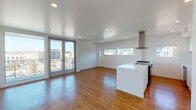Located in San Diego's vibrant Bankers Hill neighborhood, this modern unit at 915 W Grape St offers a thoughtfully designed open-concept layout bathed in natural light. Warm hardwood flooring flows seamlessly throughout the entire space, complementing the clean white walls and recessed lighting overhead.

The open living and dining area is anchored by expansive French doors leading to a private balcony, offering panoramic views of the surrounding San Diego cityscape. A wide horizontal window further enhances the connection to the outdoors, framing additional city views and flooding the space with daylight.

The contemporary kitchen is a standout feature, showcasing a sleek white island with an integrated cooktop and a stainless steel range hood above. The galley-style kitchen includes flat-front white cabinetry, a subway tile backsplash, stainless steel appliances including a refrigerator and dishwasher, and a deep undermount sink — all finished with clean, minimalist hardware.

A separate bedroom area offers a generous floor plan with large sliding glass doors opening to another outdoor balcony, maximizing natural light and views. The bathroom is finished in crisp white tones, featuring an undermount sink with quartz countertops, a large mirror, and a soaking tub with tiled surround.