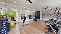 Located at 4029 Flat Shoals Pkwy in Decatur, GA, this fitness center is a thoughtfully designed exercise facility that balances functionality with modern aesthetics. The space features light hardwood flooring throughout, crisp white walls, and recessed lighting complemented by multiple ceiling fans that maintain airflow and comfort during workouts.

A standout feature is the large floor-to-ceiling mirrored wall, which visually expands the room and allows for form-checking during exercise. An eye-catching abstract wall mural adds an artistic focal point, providing visual interest against the otherwise clean, neutral palette.

The facility is well-stocked with a comprehensive range of equipment. Cardio offerings include multiple treadmills, elliptical trainers, a stair climber, and stationary bikes. A dedicated free-weight area features a full dumbbell rack, while stability and exercise balls in various sizes support stretching and functional training. A weight bench rounds out the strength-training options.

Large windows along multiple walls flood the space with natural light and offer views of the surrounding outdoor area, creating an open, energizing atmosphere. A glass-paneled door provides direct access to the exterior. The overall design is clean, modern, and inviting, offering a complete workout environment suited for a wide range of fitness routines.