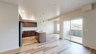 Located in Rathdrum, Idaho, this well-appointed 2-bedroom, 2-bathroom unit offers a thoughtfully designed single-level layout with modern finishes throughout. The open-concept kitchen and living area serves as the heart of the home, featuring light wood-style flooring, recessed lighting, and stylish gold pendant lights above a central island with a built-in sink and white quartz countertops. Rich, dark wood cabinetry lines the kitchen walls, complemented by a full suite of stainless steel appliances including a refrigerator, range, and microwave. A tray ceiling detail above the kitchen adds architectural interest. Sliding glass doors in the living area open to a private balcony, filling the space with natural light and providing outdoor views. The two bedrooms offer plush carpeting and textured walls, with the primary bedroom featuring a generous footprint and a large window that brings in abundant natural light. The bathrooms are finished with dark wood vanities, white quartz countertops, and clean, bright fixtures, including a tub/shower combination. Additional spaces include a room with wood-style flooring and closet access, offering flexible use. The overall ambiance is clean, bright, and move-in ready.