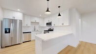 Located at 1230 E First St in Long Beach, CA, this thoughtfully designed 2-bedroom, 1-bathroom single-story home blends modern aesthetics with functional living. Light wood flooring flows consistently throughout every room, creating a cohesive and bright atmosphere. The open-concept kitchen and living area serves as the heart of the home, featuring white shaker cabinetry, a quartz waterfall island, stainless steel appliances including a gas range, built-in microwave, dishwasher, and a French door refrigerator, all accented by matte black pendant lighting. The adjacent living room is finished with soft blue-gray walls, recessed lighting, a ceiling fan, and a wall-mounted mini-split unit for efficient climate control. Both bedrooms are generously proportioned, each equipped with a ceiling fan and mini-split system, with natural light streaming in through blinded windows. The primary bedroom features mirrored sliding closet doors. A hallway connects the rooms and includes an electrical panel access. The full bathroom is finished in crisp white tile with a soaking tub, undermount sink, white shaker vanity, and matte black fixtures. Clean lines, neutral tones, and modern hardware define this move-in-ready Long Beach home.