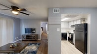 Located at 1350 Green Parkway in Houston, TX, this one-bedroom, one-bathroom unit offers a practical and well-organized single-floor layout. The open-concept living and kitchen area forms the heart of the space, where light hardwood-style flooring flows throughout. The living room is fitted with a ceiling fan, vertical blind-covered sliding doors that allow natural light, and ample room for comfortable seating arrangements. The kitchen is fully equipped with white cabinetry providing generous storage, light countertops, a built-in sink, and black appliances including a dishwasher, electric range, and refrigerator, all illuminated by overhead fluorescent lighting. A structural column separates the kitchen from the living area, adding a defined sense of zoning within the open floor plan. The bedroom features soft carpeted flooring, neutral gray walls, a window with blinds for natural light and privacy, and a dedicated closet for storage. The full bathroom is finished with wood-look tile flooring, a vanity with a single sink, a large mirror, and a tub-shower combination with a curtain enclosure. Throughout the unit, a consistent cool gray color palette creates a cohesive and calm atmosphere.