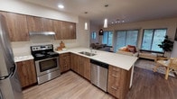 This single-floor residence at 21044 Viking Way NW, Unit 104, Poulsbo, WA offers a thoughtfully designed layout that balances modern finishes with comfortable living. The kitchen is a standout feature, showcasing wood-toned cabinetry, light quartz countertops, and a full suite of stainless steel appliances including a refrigerator, electric range, and dishwasher. Recessed lighting and pendant fixtures illuminate the space, which flows seamlessly into the open living and dining area. The living room is anchored by wide sliding glass doors that invite natural light and offer views of the surrounding greenery, creating a warm and inviting atmosphere. Wood-look flooring runs throughout the main living areas, while plush carpet adds comfort to the bedrooms. Each bedroom is a well-sized, quiet retreat with windows overlooking outdoor scenery and baseboard heating. The unit includes two bathrooms: one featuring a full soaking tub with shower, and a second with an elongated vanity and ample counter space. Dark-trimmed door frames and clean white walls provide a crisp contrast throughout. The overall design is modern, cohesive, and functional, making this a comfortable and stylish home in Poulsbo.