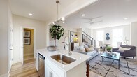 This two-story home in Gentry, Arkansas, is designed with a clean, contemporary aesthetic characterized by neutral tones, light hardwood flooring, and an abundance of natural light throughout. The main floor centers on an open-concept layout where the kitchen flows seamlessly into the living area. The kitchen is outfitted with white shaker cabinetry, quartz countertops, stainless steel appliances including a French door refrigerator and electric range, a subway tile backsplash, and a central island with an undermount sink and pendant lighting overhead. The adjacent living room features recessed lighting, a ceiling fan, and large windows that invite natural light, with a staircase fitted with modern metal cable railings serving as a visual focal point. A secondary sitting area on the main level provides additional flexible living space. The upper floor hosts multiple bedrooms, each thoughtfully appointed with recessed lighting, ceiling fans, and well-sized windows offering views of the surrounding neighborhood. A shared bathroom on the upper level features a dual-sink vanity with white cabinetry, quartz countertops, and tile flooring. Throughout both floors, the consistent use of soft neutral walls, quality finishes, and modern fixtures creates a cohesive and polished atmosphere.
