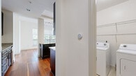 This thoughtfully designed single-floor residence offers an open-concept layout that seamlessly connects the living, dining, and kitchen areas. Rich hardwood flooring flows throughout the main living spaces, complemented by crisp white walls and an abundance of natural light streaming through large windows that frame views of lush greenery and the surrounding cityscape. A private balcony accessed via a glass door further enhances the connection to the outdoors.

The gourmet kitchen is a standout feature, appointed with dark espresso cabinetry, granite countertops, a glass tile backsplash, and a full suite of stainless steel appliances. A generous breakfast bar with pendant lighting above serves as both a functional workspace and a casual gathering spot.

The primary bedroom is a serene retreat with hardwood floors and a dedicated walk-in closet outfitted with custom shelving and hanging systems. The en-suite bathroom features a dual-sink vanity with granite counters, a glass-enclosed shower, and a soaking tub finished in neutral tile. A second bathroom mirrors the same refined aesthetic with dark cabinetry, granite counters, and a tiled shower-tub combination.

A dedicated laundry room with side-by-side washer and dryer units adds everyday convenience, while light tile flooring in the wet areas provides a clean, practical finish throughout.