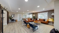 Located at 2508 Main St in Forest Grove, Oregon, this thoughtfully designed single-floor space blends modern aesthetics with a warm, welcoming atmosphere. Light wood-look flooring runs throughout, complementing neutral warm-toned walls and crisp white trim that create a cohesive, contemporary feel.

The main lounge area is generously proportioned, featuring recessed lighting, large windows with white shutters that invite abundant natural light, and an electric fireplace set into a shiplap-clad accent wall with a wood mantle — serving as a natural focal point. Cognac leather sofas, black metal accent chairs, and live-edge wood coffee tables furnish the space with a modern-rustic character.

A dedicated dining area accommodates a long communal table surrounded by metal café-style chairs, ideal for group gatherings. Adjacent to this is a hallway with a reception-style pass-through counter and seating nook, offering a more private setting.

The kitchenette is well-appointed with white shaker cabinetry, granite-look countertops, stainless steel appliances including a refrigerator, dishwasher, and microwave, along with a coffee station. A game room with a pool table rounds out the amenities, adding a recreational dimension to this versatile community space.