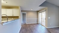 Located in Asheville, NC, this single-floor residence offers a thoughtfully designed layout with a blend of modern finishes and functional living spaces. The open living and dining area features rich wood-look flooring, neutral wall tones with a two-tone paint treatment, and a sliding glass door that provides direct access to a private outdoor deck, filling the space with natural light and wooded views. The living area extends into a carpeted lounge space with a vaulted ceiling, ceiling fan, a large window, and a built-in shelving unit with cabinetry — a distinctive architectural detail that adds both character and storage. The kitchen is well-equipped with white shaker-style cabinetry, granite-look countertops, stainless steel appliances including an electric range, and a pass-through to the living area. The bedrooms are carpeted and bright, each featuring windows with wooded outdoor views, offering a peaceful retreat. The bathroom includes a full tub-shower combination with clean, classic fixtures and wood-look flooring. A dedicated laundry room with a full-size washer and dryer adds everyday convenience. Throughout, textured ceilings and consistent neutral finishes contribute to a cohesive, move-in-ready aesthetic.