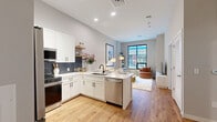 Located at 1201 Constitution Ave in Philadelphia, this thoughtfully designed one-bedroom, one-bathroom residence offers a efficient and well-appointed living space. The open-concept layout seamlessly connects the kitchen and living room, creating an inviting and functional flow throughout.

The kitchen is a standout feature, showcasing crisp white shaker cabinetry, a striking navy hexagonal tile backsplash, white quartz countertops, stainless steel appliances including a French door refrigerator, dishwasher, and range, along with open floating shelves for added character.

The living room is bright and airy, anchored by large black-framed windows that frame urban views of the surrounding Philadelphia cityscape and fill the space with natural light. Warm hardwood-style flooring runs throughout the main living areas, lending a cohesive and polished look.

The bedroom is a comfortable retreat featuring plush carpeting, a large window with city views, and ample closet space — with three closets total providing generous storage throughout the residence. The bathroom is finished with a white vanity, hardwood-style flooring, and a tub-shower combination. A dedicated utility room completes the layout, adding everyday practicality to this modern urban home.