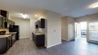 This single-story unit at The Foundry offers a well-organized layout designed for comfortable, functional living. The galley-style kitchen is a standout feature, lined on both sides with dark espresso cabinetry, granite-style countertops, and black appliances including a refrigerator, range, and dishwasher. Light wood-style flooring runs throughout the kitchen and living areas, providing a clean, cohesive aesthetic.

The open living and dining area is generously proportioned, bathed in natural light from a large window and a glass door that leads directly to a private balcony, offering outdoor views of the surrounding community. Neutral, warm-toned walls complement the flooring throughout, creating a calm and welcoming ambiance.

The bedrooms are carpeted for comfort and feature ample closet space with built-in hanging rods. Natural light filters in through blinds-covered windows, contributing to a bright atmosphere. The bathrooms are finished consistently with the kitchen, featuring dark vanity cabinetry, granite-style countertops, framed mirrors, and full-size tub and shower combinations with wood-style flooring. The overall design balances practicality with modern finishes throughout.
