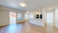 This thoughtfully laid-out single-floor residence offers a comfortable and efficient use of space across one bedroom, one bathroom, and several well-defined areas. The open-concept living and kitchen area forms the heart of the home, featuring light wood-style flooring that creates a bright and cohesive feel throughout. Large windows dressed with vertical blinds allow natural light to fill the space, while a sliding door provides direct access to an outdoor area, enhancing the sense of openness.

The kitchen is positioned along a peninsula layout with light wood cabinetry, a white countertop, and black appliances including a refrigerator, range, and microwave. Track lighting overhead and a built-in sink along the peninsula add to its functional design. The living area is generously proportioned, offering flexibility for various furniture arrangements.

The bedroom is carpeted for comfort and features two windows that bring in natural light. A wall-mounted mini-split HVAC unit ensures individual climate control. A dedicated closet provides organized storage adjacent to the room.

The bathroom is clean and functional, featuring a full tub-shower combo, light wood-style flooring, and a vanity with a white countertop. A dedicated laundry room with side-by-side washer and dryer units and overhead wire shelving adds everyday convenience to this well-appointed residence.