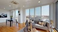 This contemporary single-floor residence is defined by its striking floor-to-ceiling window walls in the living area, which flood the space with natural light and frame expansive panoramic views of the surrounding cityscape. The open-concept living and dining area showcases warm hardwood flooring that runs throughout the unit, creating a cohesive and inviting aesthetic. A cassette-style HVAC unit is integrated into the ceiling, complementing the clean, modern design.

The kitchen is well-appointed with two-tone cabinetry — white upper cabinets paired with gray lower cabinets — along with a full suite of stainless steel appliances including a gas range, hood, dishwasher, and French-door refrigerator. Light countertops complete the contemporary look.

Multiple bedrooms offer hardwood floors, bright windows with urban views, and a calm, neutral palette. One bedroom features a large sliding glass door opening to an outdoor space.

Two bathrooms are finished with wood-look porcelain tile flooring and crisp white walls. The primary bath includes a soaking tub with a glass enclosure and striking wood-toned tile surround, while the secondary bath features a wall-mounted vanity and glass shower enclosure.