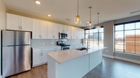 Located in the heart of downtown Columbus at 205 S High St, this single-floor unit offers a sleek, modern aesthetic with an open-concept design that seamlessly connects the kitchen and living areas. The kitchen is a standout feature, boasting white shaker-style cabinetry extending to the ceiling, light quartz countertops, a large center island with an undermount sink, and a full suite of stainless steel appliances including an electric range, microwave, dishwasher, and refrigerator. A subway tile backsplash and globe pendant lights add a contemporary, polished touch. Large black-framed floor-to-ceiling windows flood the living area with natural light and frame views of the surrounding Columbus skyline and cityscape. The open living space is finished with durable wood-style flooring that runs throughout, complemented by neutral-toned walls. A dedicated laundry area includes a stacked full-size washer and dryer unit with built-in shelving for added storage convenience. A bathroom features wood-style flooring and chrome fixtures. The overall ambiance is clean, bright, and contemporary, offering a refined urban living experience in one of Columbus's most vibrant downtown locations.