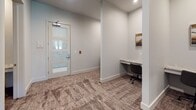 Located at 9102 FM 2920 in Tomball, Texas, this single-floor professional business center is thoughtfully designed to support a range of work needs. The space features a dedicated conference room anchored by a substantial dark-wood rectangular table surrounded by upholstered seating for multiple attendees. A brass-toned geometric chandelier with glass pendants serves as the room's focal point, complementing neutral walls and roller-shade windows that allow natural light to filter in while maintaining privacy. Framed artwork, including a striking black-and-white railway photograph, adds visual interest throughout.

Adjacent to the conference room, a corridor leads to multiple individual workstations built into alcoves along the walls. Each station is equipped with a marble-topped desk surface and an ergonomic rolling chair, with curated artwork above each workspace to foster an inspiring environment. The workstations are separated by a structural column, providing a sense of privacy between users.

Textured, earth-toned carpet runs throughout the space, adding warmth and acoustic comfort. A glass-paneled entry door with frosted detailing provides both security and an open, airy feel to the entryway. Overall, the space balances a clean, modern aesthetic with functional design, making it well-suited for focused individual work and collaborative meetings alike.