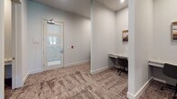 Located at 9102 FM 2920 in Tomball, Texas, this single-floor professional business center is thoughtfully designed to support a range of work needs. The space features a dedicated conference room anchored by a substantial dark-wood rectangular table surrounded by upholstered seating for multiple attendees. A brass-toned geometric chandelier with glass pendants serves as the room's focal point, complementing neutral walls and roller-shade windows that allow natural light to filter in while maintaining privacy. Framed artwork, including a striking black-and-white railway photograph, adds visual interest throughout.

Adjacent to the conference room, a corridor leads to multiple individual workstations built into alcoves along the walls. Each station is equipped with a marble-topped desk surface and an ergonomic rolling chair, with curated artwork above each workspace to foster an inspiring environment. The workstations are separated by a structural column, providing a sense of privacy between users.

Textured, earth-toned carpet runs throughout the space, adding warmth and acoustic comfort. A glass-paneled entry door with frosted detailing provides both security and an open, airy feel to the entryway. Overall, the space balances a clean, modern aesthetic with functional design, making it well-suited for focused individual work and collaborative meetings alike.