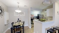 This single-floor residence offers a thoughtfully designed layout that balances comfort and functionality. Light wood-style flooring flows seamlessly throughout the unit, creating a cohesive and inviting atmosphere.

The open-concept kitchen is equipped with stainless steel appliances, including a range and refrigerator, complemented by crisp white cabinetry and a decorative tile backsplash. A breakfast bar with seating provides a casual dining option, while the adjacent dining area accommodates a full dining table beneath a pendant light fixture — ideal for everyday meals and entertaining.

The living room is generously proportioned, featuring a ceiling fan and large windows that allow ample natural light to fill the space. The layout comfortably accommodates a large sectional sofa and additional seating.

Two well-sized bedrooms each include ceiling fans and walk-in closets, offering practical storage solutions. Both bathrooms are finished with white vanities, tub-shower combinations, and wood-style flooring, maintaining the clean and consistent aesthetic found throughout the residence.

The overall design is neutral and bright, with light gray and beige tones on the walls, creating a versatile backdrop suitable for a range of interior styles.