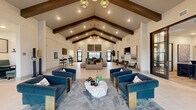 Located at 5697 SW 49th Rd in Ocala, Florida, this single-floor community clubhouse is a thoughtfully designed gathering space that blends modern farmhouse aesthetics with contemporary comfort. The centerpiece of the space is its dramatic vaulted ceiling adorned with bold, dark-stained exposed wood beams, which lend warmth and architectural character throughout.

Large format light-toned tile flooring extends across the open layout, creating a clean and cohesive foundation. The main living area is anchored by plush navy blue velvet armchairs and a striking natural stone coffee table, all set atop a layered area rug that defines the central lounge zone. Pendant lighting fixtures with a warm metallic finish hang overhead, complementing the recessed lighting that illuminates the space evenly.

Floor-to-ceiling black-framed windows and glass entry doors line the perimeter, inviting generous natural light and offering views of the surrounding landscape. A wainscoted accent wall showcases framed artwork and a mounted television, flanked by additional seating clusters with sleek leather chairs and minimalist side tables.

A casual dining area features tufted booth seating alongside bar-height tables, while a separate workspace zone with glass-partitioned walls provides a more focused environment. The overall ambiance is refined yet welcoming, making this a versatile and well-appointed communal facility.