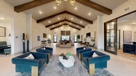 Located at 5697 SW 49th Rd in Ocala, Florida, this single-floor community clubhouse is a thoughtfully designed gathering space that blends modern farmhouse aesthetics with contemporary comfort. The centerpiece of the space is its dramatic vaulted ceiling adorned with bold, dark-stained exposed wood beams, which lend warmth and architectural character throughout.

Large format light-toned tile flooring extends across the open layout, creating a clean and cohesive foundation. The main living area is anchored by plush navy blue velvet armchairs and a striking natural stone coffee table, all set atop a layered area rug that defines the central lounge zone. Pendant lighting fixtures with a warm metallic finish hang overhead, complementing the recessed lighting that illuminates the space evenly.

Floor-to-ceiling black-framed windows and glass entry doors line the perimeter, inviting generous natural light and offering views of the surrounding landscape. A wainscoted accent wall showcases framed artwork and a mounted television, flanked by additional seating clusters with sleek leather chairs and minimalist side tables.

A casual dining area features tufted booth seating alongside bar-height tables, while a separate workspace zone with glass-partitioned walls provides a more focused environment. The overall ambiance is refined yet welcoming, making this a versatile and well-appointed communal facility.