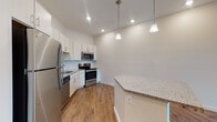 This well-appointed single-floor unit offers a thoughtfully designed layout that blends functionality with modern aesthetics. The open-concept kitchen serves as a central highlight, showcasing crisp white and light wood cabinetry, granite countertops, and a herringbone-patterned tile backsplash. A full suite of stainless steel appliances — including a refrigerator, electric range, over-the-range microwave, and dishwasher — completes the space, while a kitchen island provides additional prep and seating space. Pendant lighting above the island adds a polished finishing touch. Warm hardwood-style flooring flows throughout the kitchen and main living areas, lending a cohesive and inviting feel. The living room is generously proportioned, featuring a ceiling fan, large windows dressed with blinds, and a private exterior door that allows natural light to fill the space. The bedroom offers plush carpeting, a ceiling fan, a well-sized window, and a walk-in closet equipped with wire shelving for organized storage. The bathroom is cleanly finished with a granite-topped vanity with light wood cabinetry, a tiled shower-tub combination, and light flooring. Throughout, the unit maintains a clean, neutral palette that creates a bright and welcoming atmosphere.
