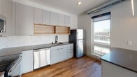 Located at 453 Snelling Ave N in Saint Paul, Minnesota, this modern single-floor unit offers a thoughtfully designed layout with contemporary finishes throughout. The kitchen serves as a standout feature, showcasing flat-front gray cabinetry reaching the ceiling, open wood-accented shelving, and a bold hexagonal tile backsplash. Stainless steel appliances — including a refrigerator, dishwasher, electric range, and over-the-range microwave — complement the dark countertops, while a large window floods the space with natural light and offers views of the surrounding neighborhood. Warm hardwood-style flooring runs throughout the main living areas, adding a cohesive and inviting feel. A central hallway connects the various rooms with ease, providing access to the bathroom and additional living spaces. The bathroom is clean and functional, featuring a full soaking tub with shower, a white vanity with ample drawer storage, and wood-style flooring that continues the unit's consistent aesthetic. A dedicated walk-in closet with built-in shelving and rod provides generous storage capacity. The overall design emphasizes a bright, minimalist aesthetic with white walls, recessed lighting, and an open, airy atmosphere ideal for modern living.