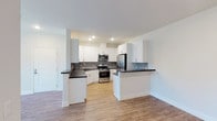 Located at 21595 Box Springs Rd in Moreno Valley, California, this single-floor residence offers a clean, modern aesthetic throughout. The open-concept kitchen is a standout feature, showcasing crisp white shaker cabinetry, dark quartz countertops, a grey tile backsplash, and a full suite of stainless steel appliances including a gas range, built-in microwave, and French door refrigerator. Light wood-style flooring flows through the kitchen and living areas, lending warmth and continuity to the space. A peninsula counter provides additional prep space and naturally defines the transition to the living area. The bedrooms are finished with plush wall-to-wall carpeting and feature windows with blinds that allow for natural light and outdoor views. The primary bedroom is generously sized, offering access to a dedicated walk-in closet and an en-suite bathroom equipped with a dual-sink vanity, dark countertops, and wood-look flooring. A secondary bathroom features a single-sink vanity with dark countertops and a full tub-shower combination. Throughout the residence, a neutral color palette, recessed lighting, and clean white walls create a bright, move-in-ready atmosphere suited for comfortable everyday living.