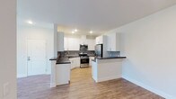 Located at 21595 Box Springs Rd in Moreno Valley, California, this single-floor residence offers a clean, modern aesthetic throughout. The open-concept kitchen is a standout feature, showcasing crisp white shaker cabinetry, dark quartz countertops, a grey tile backsplash, and a full suite of stainless steel appliances including a gas range, built-in microwave, and French door refrigerator. Light wood-style flooring flows through the kitchen and living areas, lending warmth and continuity to the space. A peninsula counter provides additional prep space and naturally defines the transition to the living area. The bedrooms are finished with plush wall-to-wall carpeting and feature windows with blinds that allow for natural light and outdoor views. The primary bedroom is generously sized, offering access to a dedicated walk-in closet and an en-suite bathroom equipped with a dual-sink vanity, dark countertops, and wood-look flooring. A secondary bathroom features a single-sink vanity with dark countertops and a full tub-shower combination. Throughout the residence, a neutral color palette, recessed lighting, and clean white walls create a bright, move-in-ready atmosphere suited for comfortable everyday living.