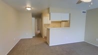 This single-floor residence in Texarkana offers a practical and comfortable layout designed for everyday living. The open-concept living area features neutral-toned carpet that extends throughout, creating a warm and cohesive feel across the main spaces. The kitchen is positioned adjacent to the living area and is defined by a peninsula-style breakfast bar that serves as both a functional workspace and a natural divider between the two areas. White upper cabinetry lines the kitchen walls, providing ample storage, while the light-colored countertops and white appliances contribute to a clean, bright aesthetic. The kitchen is well-lit and includes a sink along the bar counter, making it both efficient and accessible. A central hallway connects the living and kitchen area to the remaining rooms of the residence, with doors visible leading to additional private spaces. The walls throughout are finished in a soft, warm neutral tone that complements the carpeted flooring. Flush-mounted ceiling lighting provides consistent illumination throughout the main living space. Overall, the layout is straightforward and functional, with a cohesive design that emphasizes ease of movement and practical use of space.