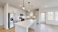 Located in Spring Hill, Tennessee, this well-appointed single-story home offers two bedrooms, two bathrooms, and two closets within a thoughtfully designed floor plan. The open-concept kitchen and living area serves as the heart of the home, showcasing white shaker cabinetry, a classic subway tile backsplash, stainless steel appliances, and a central island with a built-in wine rack, all illuminated by stylish pendant lighting. Light hardwood-style flooring flows throughout the main living areas, lending a clean, modern aesthetic. The living room is bathed in natural light through multiple windows, with views of the surrounding outdoor scenery. The spacious primary bedroom features plush carpeting, a ceiling fan, dual windows with outdoor views, and direct access to a well-designed ensuite bathroom. The primary bath includes a dual-sink vanity with sleek matte black fixtures, a walk-in tiled shower, and an adjoining walk-in closet with built-in shelving and hanging rods. The second bedroom also offers hardwood-style flooring and ample natural light from multiple windows. A bright, clean hallway connects all rooms seamlessly, completing this move-in-ready home with a fresh, contemporary feel.