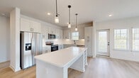 Located in Spring Hill, Tennessee, this well-appointed single-story home offers two bedrooms, two bathrooms, and two closets within a thoughtfully designed floor plan. The open-concept kitchen and living area serves as the heart of the home, showcasing white shaker cabinetry, a classic subway tile backsplash, stainless steel appliances, and a central island with a built-in wine rack, all illuminated by stylish pendant lighting. Light hardwood-style flooring flows throughout the main living areas, lending a clean, modern aesthetic. The living room is bathed in natural light through multiple windows, with views of the surrounding outdoor scenery. The spacious primary bedroom features plush carpeting, a ceiling fan, dual windows with outdoor views, and direct access to a well-designed ensuite bathroom. The primary bath includes a dual-sink vanity with sleek matte black fixtures, a walk-in tiled shower, and an adjoining walk-in closet with built-in shelving and hanging rods. The second bedroom also offers hardwood-style flooring and ample natural light from multiple windows. A bright, clean hallway connects all rooms seamlessly, completing this move-in-ready home with a fresh, contemporary feel.