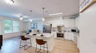 Located at 7300 Ashlake Pkwy in Chesterfield, VA, this one-bedroom, one-bathroom residence offers a thoughtfully designed single-floor layout with modern finishes throughout. The open-concept kitchen and living area serves as the heart of the home, featuring light hardwood-style flooring, crisp white shaker cabinetry, granite countertops, and a central island with bar seating illuminated by pendant lighting. Stainless steel appliances — including a French door refrigerator, electric range with hood, and built-in microwave — complete the well-equipped kitchen, which also includes a convenient built-in desk area. The adjoining living room is bright and welcoming, with large windows that invite natural light and views of the outdoors, complemented by a ceiling fan overhead. The bedroom offers plush carpeting, multiple windows, a ceiling fan, and generous closet storage. The full bathroom is finished with tile flooring, a granite-topped vanity with white cabinetry, and a combination tub and shower. Additional conveniences include an in-unit laundry area and three closets for ample storage. The residence presents a clean, contemporary aesthetic with a neutral color palette throughout.