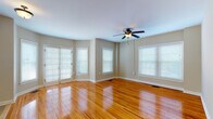 This single-floor space is thoughtfully laid out, offering a cohesive blend of functional design and warm finishes throughout. The living area is a standout feature, characterized by richly polished hardwood floors that reflect abundant natural light streaming in through multiple large windows fitted with white blinds. A ceiling fan with a built-in light fixture anchors the room, and a set of French doors provides additional access and light. The neutral taupe walls complement the warm wood tones, creating an inviting and airy atmosphere.

An elegant arched passageway connects the living area to the kitchen, adding a refined architectural detail to the space. The kitchen is well-equipped, featuring rich dark-stained wood cabinetry, granite-style countertops, a stainless steel double sink, and a full suite of black appliances including a range, built-in microwave, dishwasher, and refrigerator. Tile flooring grounds the kitchen area, providing a practical contrast to the hardwood elsewhere.

The bedroom continues the hardwood flooring and multi-window design, maintaining a bright and open feel. The bathroom offers a clean, functional layout with a dark wood vanity, white countertop, tiled shower with glass doors, subway-tiled walls with accent trim, and a window for natural ventilation.